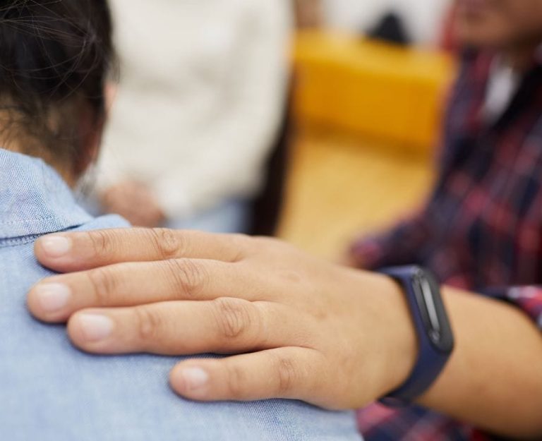 A close up of a hand on another person's shoulder offering support.